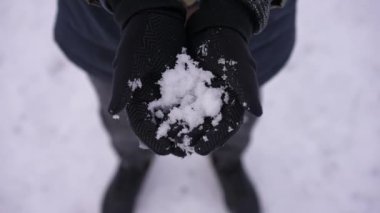 High angle view white snow in black mittens outdoors. Close-up unrecognizable boy holding snowball showing in slow motion. Weather and season concept