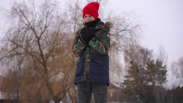 寒い冬の日に屋外に立って手をこすりヤシの上に吹いて凍結白人の十代の少年 10代の曇りの日に待っている スローモーション — ストック動画