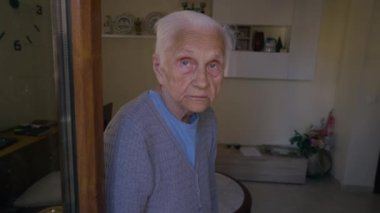 Grey-haired old Caucasian woman looking away smiling standing at home indoors. Portrait of positive senior female retiree in room