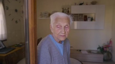 Portrait of senior wrinkled retiree sitting indoors looking around. Caucasian old woman with grey hair and grey eyes resting at home. Comfort and aging concept