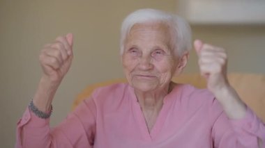 Laughing grey-haired happy old woman gesturing success looking around sitting on armchair indoors. Portrait of cheerful relaxed Caucasian senior retiree rejoicing gesturing