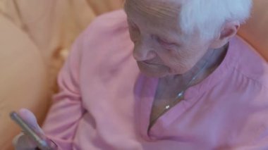 Top view old Caucasian woman gesturing watching online match on smartphone. Portrait of senior wrinkled sports fan rejoicing supporting team. Modern technologies and hobbies concept