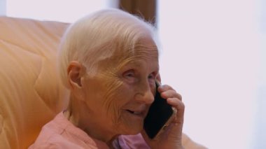 Happy senior female retiree laughing talking on phone sitting indoors. Portrait of joyful Caucasian old woman chatting smiling enjoying leisure at home