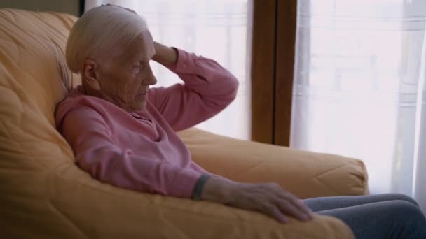 一位心烦意乱的白种人白发苍苍的老妇人坐在扶手椅上 一边说着话 一边看风景 深谋远虑的退休人员靠扶手动脑子思考 — 图库视频影像