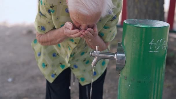 暑い夏の日に屋外の蛇口から古い白髪の女性が水を飲んでいます 南の国で観光旅行を楽しむシニア白人退職者 — ストック動画