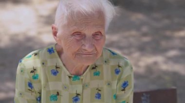 Depressed wrinkled female retiree thinking sitting outdoors on sunny summer day. Portrait of grey-haired Caucasian senior woman in park. Frustration and lifestyle concept