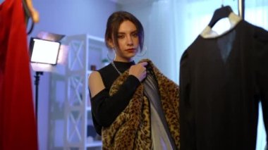 Young attractive slim woman choosing fur coat in slow motion trying on clothes standing indoors. Medium shot portrait of brunette Caucasian lady with brown eyes thinking making decision on style