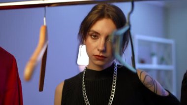 Portrait of self assured gorgeous young slim woman looking at camera standing at rack with coat hangers. Beautiful Caucasian millennial lady posing in slow motion indoors at home