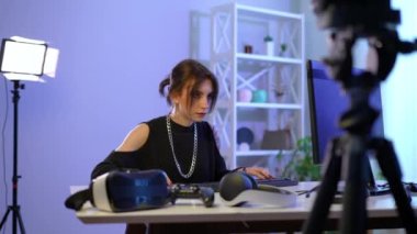 Portrait of focused serious slim beautiful woman gaming online filming video blog. Medium shot of concentrated absorbed Caucasian gamer playing with keyboard and mouse on PC sitting at table