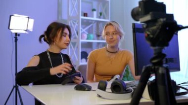 Two confident female gamers greeting subscribers talking start gaming on PC. Positive beautiful Caucasian young women playing online sitting at table indoors