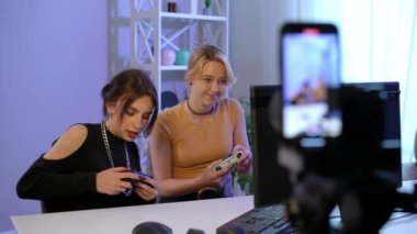 Two young absorbed women gaming online losing filming video blog indoors. Beautiful Caucasian millennial bloggers playing games on PC with joysticks filming vlog