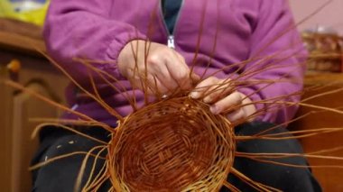 Unrecognizable plus-size woman inserting strand in round-shaped wicker basket base sitting indoors. Front view talented Caucasian lady making handmade decoration