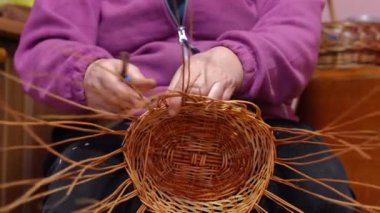 Close-up brown wicker basket with female hands designing shape. Unrecognizable Caucasian confident skilled woman making handmade decoration indoors