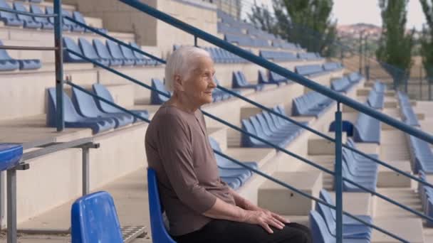 Side View Old Curios Woman Sitting Tribune Stadium Looking Away — Vídeo de Stock