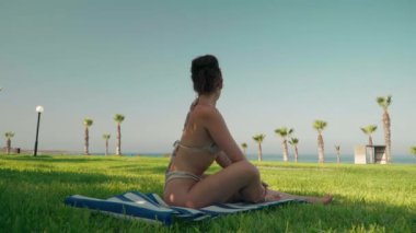 Side view motivated slim sportswoman in bikini warming up leg muscles admiring Mediterranean sea. Wide shot tanned confident Caucasian young woman training outdoors enjoying healthy lifestyle