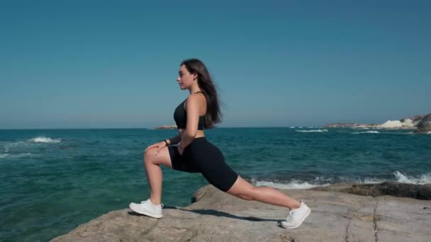 サイドビュー地中海で岩の上に立って肺を行う豪華なスポーツウーマン ワイドショットフィット白人若いですスリム女性ワークアウトトレーニング屋外でキプロス — ストック動画