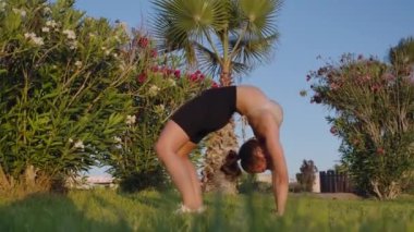 Side view backbend of flexible fit sportswoman at sunset outdoors. Wide shot Caucasian slim gorgeous woman working out exercising at sundown on backyard