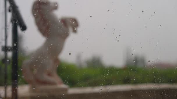 雨は左側の背景にぼやけた馬の彫刻でガラスの上に落ちる キプロス島の雨の日屋外 — ストック動画