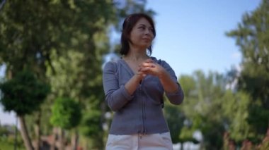 Kendine güveni tam bir kadın portresi dışarı çıkıp el kaslarını ısıtıyor ve gidiyor. Güler yüzlü beyaz kadın yaz güneşli bir günde parkta antrenman yapıyor.