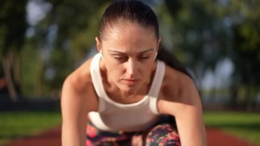 Kendine güvenen konsantre sporcu kadının yakın plan portresi başlangıç çizgisinde kameraya yavaş çekimde bakıyor. Ön manzara, güneş batarken spor pistinde poz veren Kafkas formda bir kadın.