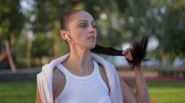 Genç, kendine güvenen bir kadın spor pistinde durup gülümsüyor ve yavaş çekimde ferahlatıcı su içiyor. Açık havada antrenman yapmaktan hoşlanan sağlıklı beyaz kadın portresi.