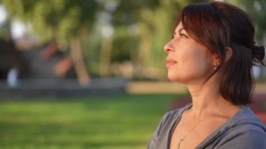 Güzel, kızıl saçlı, beyaz kadın gün batımını izlerken gözlerini açıyor ve kameraya bakıyor. Gün batımında parkta yavaş çekimde poz veren kendine güvenen çekici bir kadının portresi.