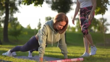 Geniş açı, yoğun konsantrasyonlu pozitif kadın dışarıda, güneş ışığında, koç yaklaşırken konuşuyor. Gün batımında antrenörle parkta antrenman yapan kendine güvenen beyaz kadın.