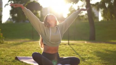 Dışarıdaki güneş ışınlarında gerinerek gülümseyen genç, sıska yogi 'nin geniş açılı portresi. Parkta günbatımında antrenmanların keyfini çıkaran kendine güveni tam beyaz bir sporcu. Yavaş çekim