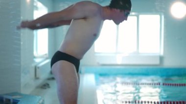 Yan manzara genç adam havuz başında havuz başında egzersiz yapıyor. Beyaz tenli sporcu yüzücü yüzme havuzunda antrenman yapıyor. Kas ısıtıyor, el büküyor.