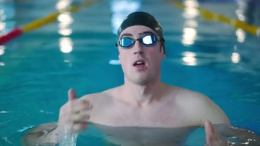 Yüzme havuzunda yüzen genç bir sporcunun portresi. Ön manzara, gözlüklü ve ağır çekimde yarışma için şapka eğitimi alan Kafkasyalı motivasyonlu bir adam.