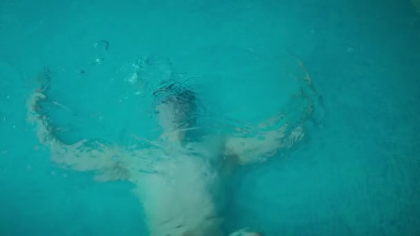 蓝色的水 有气泡和无法辨认的游泳者在游泳池的水下 年轻的白人男子躺在底部训练耐力 慢动作 — 图库视频影像