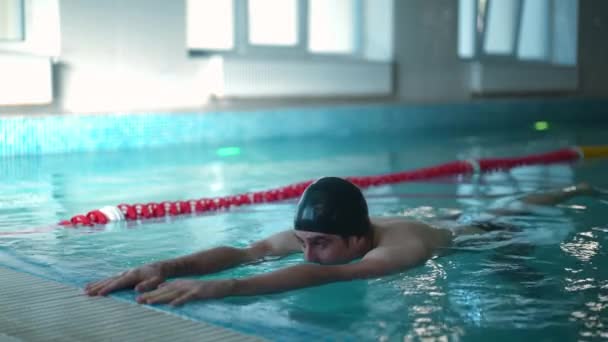 在游泳池的水里运动的专注的 有动机的白人游泳运动员 年轻自信的运动员在黑暗中在室内训练的肖像 慢动作 — 图库视频影像
