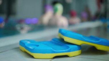 Yüzme havuzunda, arka planda tanınmayan çocukların yavaş çekimde sıçradığı yakın plan yüzülebilir oyuncaklar. Bir grup beyaz çocuk içeride yüzmeyi öğreniyor.
