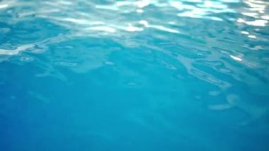 Kapalı alanda güneş ışığıyla yakın plan mavi su. Yüzme havuzunda hiç insan yok.