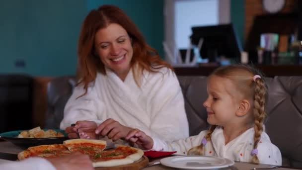 母としてSpaレストランのテーブルに座って興奮かなり娘は プレート上にピザスライスを配置します 両親と屋内でレジャーを楽しむ幸せな満足少女の肖像画 — ストック動画