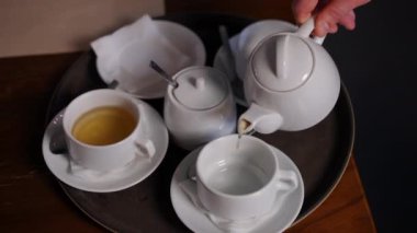 Yakından erkek eli çaydanlıktan fincanlara yeşil bitki çayı dolduruyor. Restorandaki kafede sıcak içecek servisi yapan tanınmayan profesyonel garson.