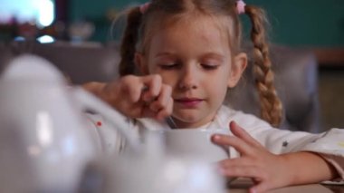 Çay fincanında şeker karıştıran, gülümseyen, konuşan sevimli beyaz kızın yakın plan portresi. Şirin çocuk kaşık yalıyor. Lokanta kafeteryasında lezzetli sıcak içkinin tadını çıkarıyor.