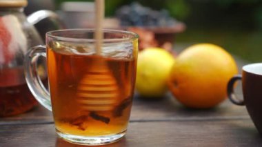 Şeffaf cam çay bardağında lezzetli içecekle karıştırılmış bal kaşığı. Beyaz kadın eli, sonbahar günü açık havada tatlı nektarla lezzetli bitkisel sıcak içeceği karıştırıyor.