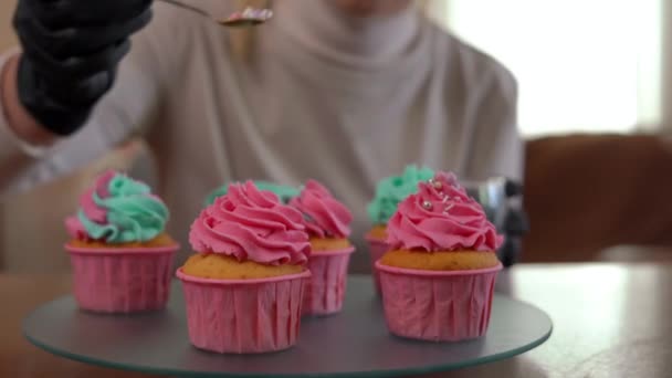 模糊的无法辨认的糖果装饰松饼与粉红玫瑰糖球结冰 在室内烘焙美味糕点的白人年轻女子微笑着 — 图库视频影像