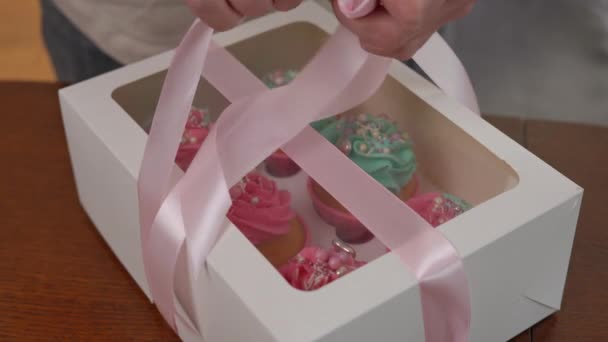 Крупным Планом Женские Руки Завязывают Розовую Ленту Бумажной Коробке Кексами — стоковое видео