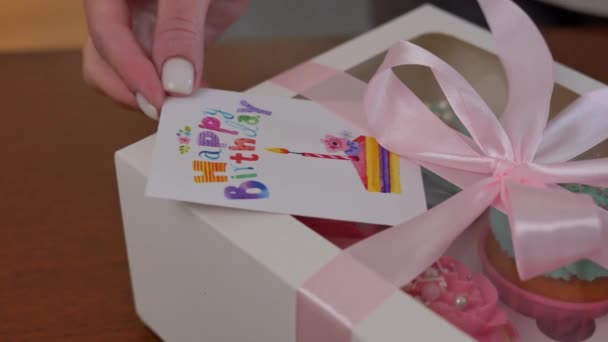 女性的手把生日快乐贺卡放在纸盒上 并配上美味的糕点 无法辨认的糖果商在家里的面包店里准备惊喜礼物 — 图库视频影像