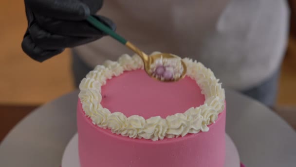 将可食用珍珠洒在奶油奶油上 并在室内烘烤粉红蛋糕上 高角镜特写无法辨认的女糖果师装饰美味甜饼 — 图库视频影像