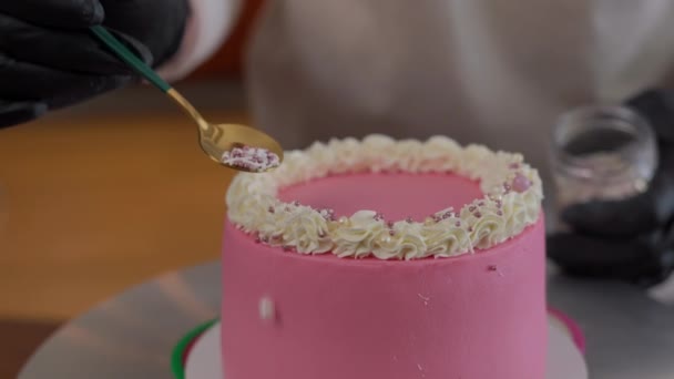 在圆形粉红蛋糕上涂有白色奶油装饰的可食用珍珠 室内特写装饰美味糕点的难以辨认的女人 — 图库视频影像