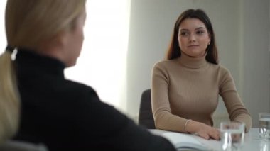 Masada terapistle otururken gülümseyen genç bir kadın. Atamada uzman psikologları dinleyen beyaz bir hastanın portresi.