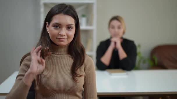 セラピスト事務所の左側に座っているカメラに触れる髪を見ている美しい若い女性 — ストック動画