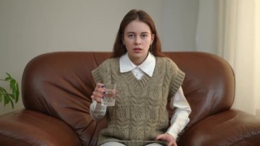 Ön manzara, elinde bir bardak suyla kameraya bakan ürkek genç kızı korkuttu. İçerde poz veren korkmuş beyaz gencin orta boy portresi.