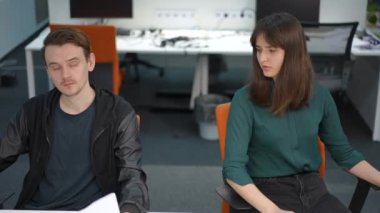 Önden bakan zeki genç adam ve kadın ofiste iş konuşuyorlar. Kafkasyalı meslektaşlarının orta boy portresi başlangıç planını anlatıyor