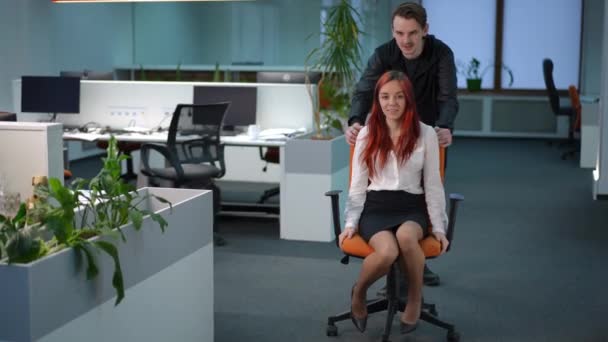 一个微笑的男人和一个快乐的年轻女人坐在办公室椅子上 慢吞吞地离去 无忧无虑的白种人同事在室内玩乐 — 图库视频影像