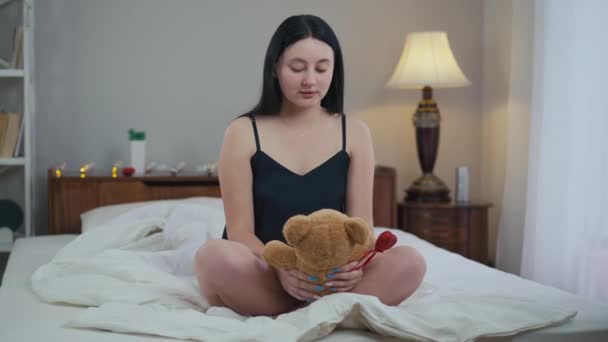 穿着睡衣的大个子瘦小女人坐在床上抱着泰迪熊 把目光移开 早上在家卧室里拿着玩具的白人女士的画像 — 图库视频影像
