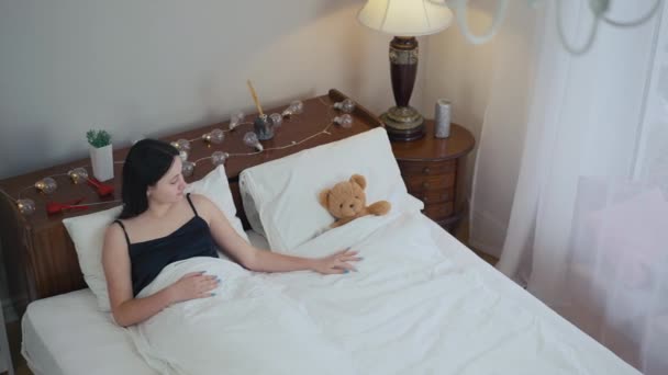 高角镜孤独的年轻女子躺在床上 带着泰迪熊的想法 早上在卧室里用玩具娃娃吸引白人女士 — 图库视频影像